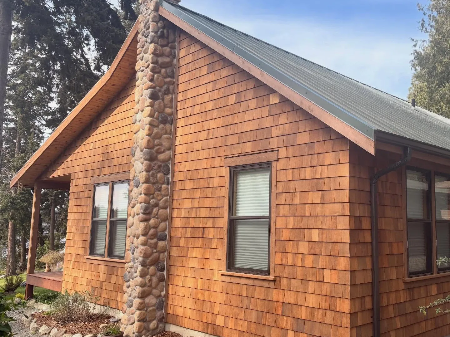 Cedar shingle cabin with a stone chimney and a green metal roof