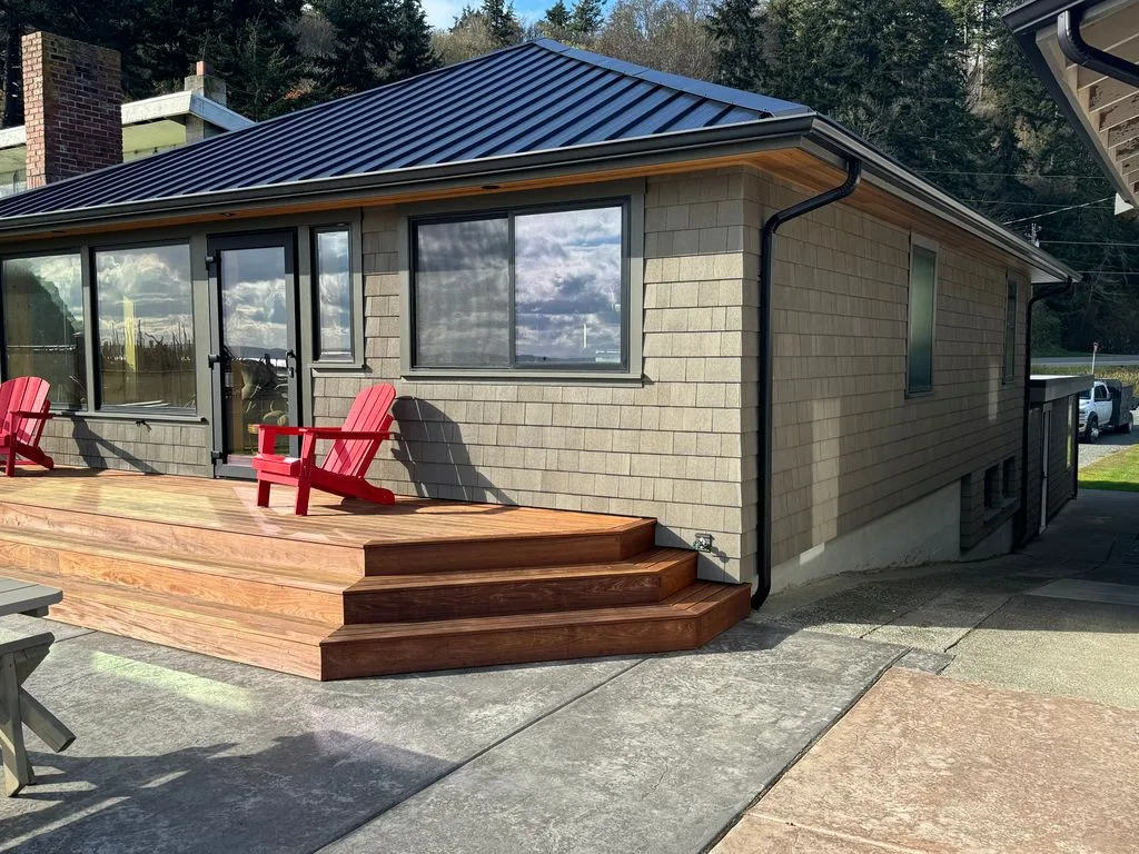Remodeled home with new cedar shingle siding, a black metal roof and a deck with red chairs