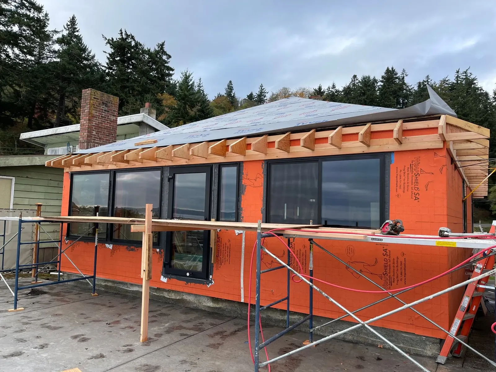 Cottage remodel in progress with house wrap, new windows and new rafter tails under scaffolding