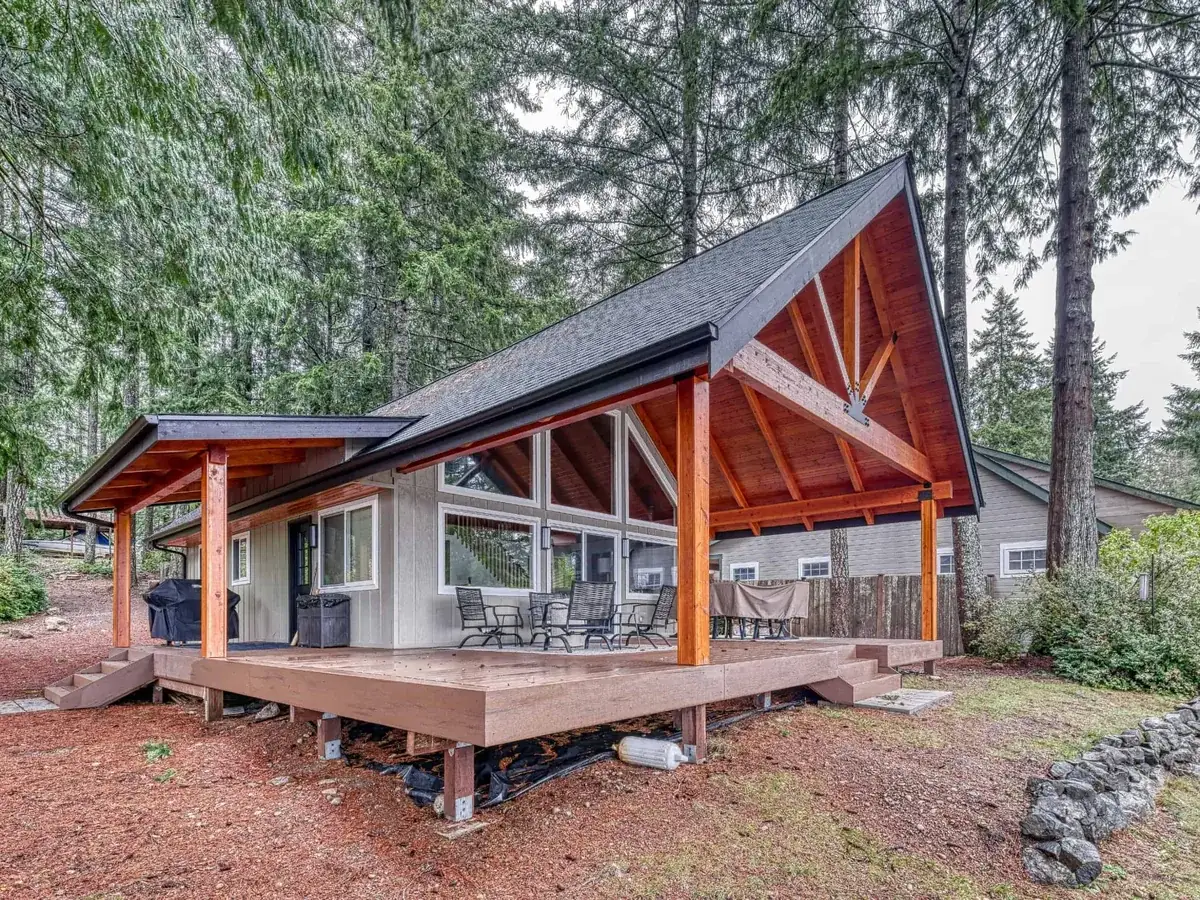 Covered deck with a gable roof on timber posts beside a house in the trees