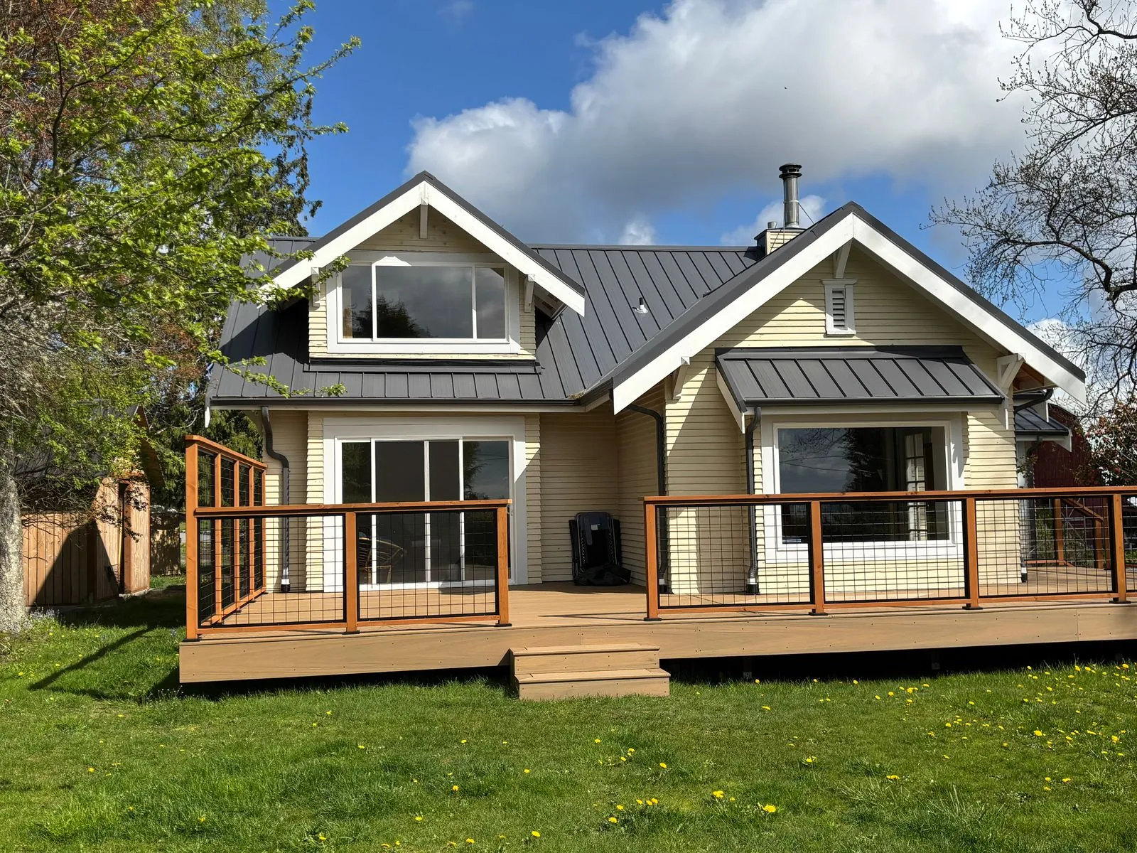 Cream house with a dark standing-seam metal roof and a deck with cable railing