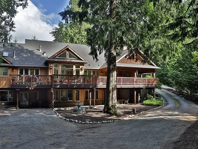 Custom home with cedar shingle gables and a wraparound deck at the end of a gravel drive