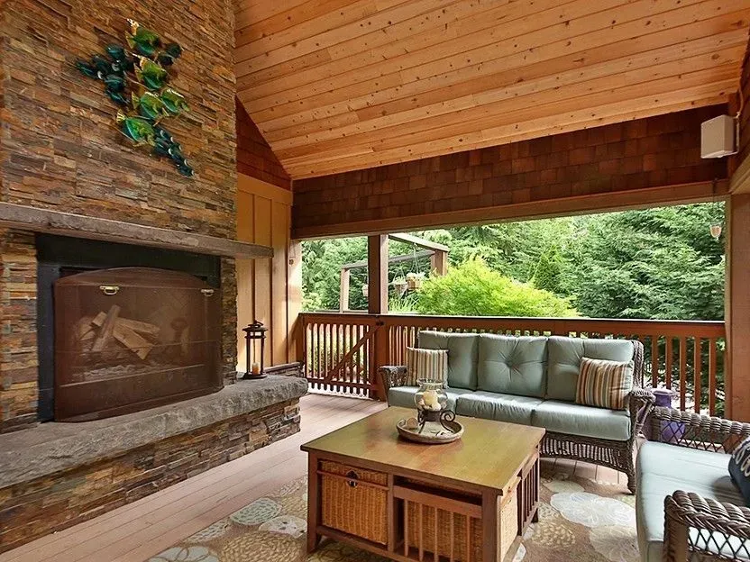 Covered porch with a stone fireplace and a cedar ceiling on a custom home