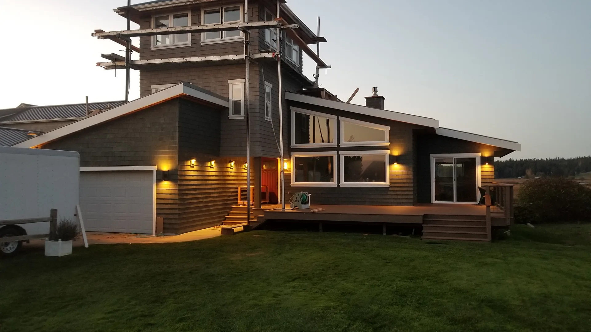 Custom home with a lookout tower and lit windows at dusk on Whidbey Island