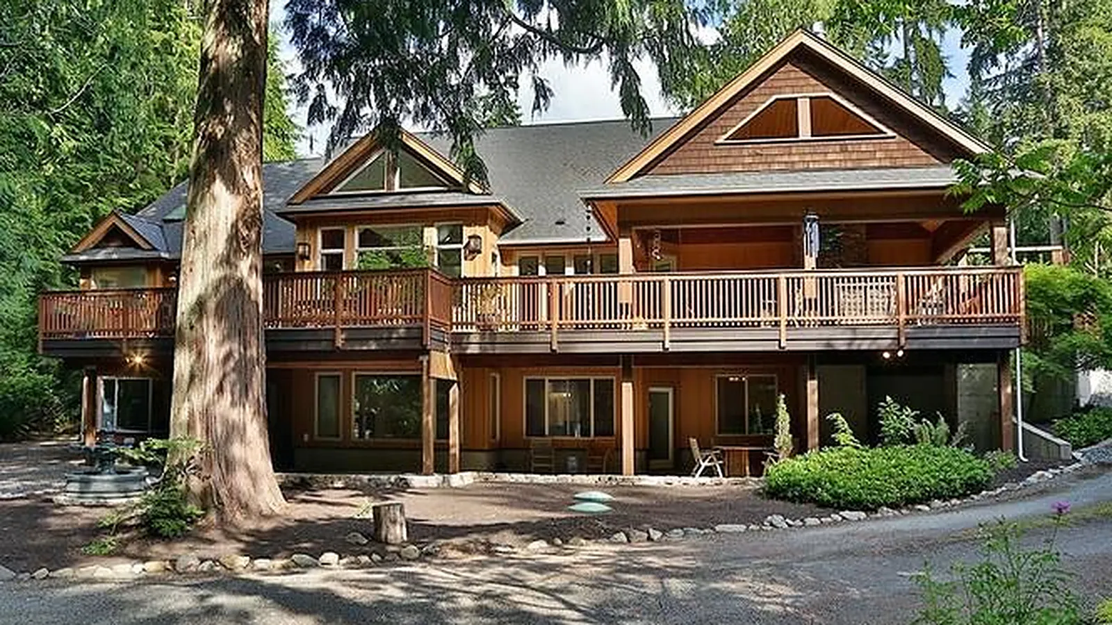 Custom home with cedar shingle gables and a long deck, set among tall evergreens