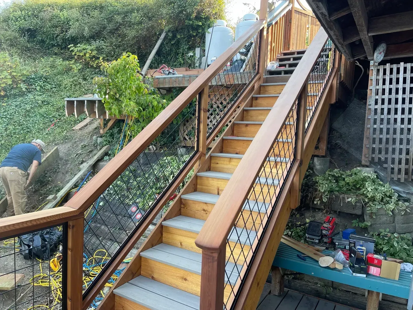 New deck stairs with a wood handrail and wire panel railing climbing a hillside