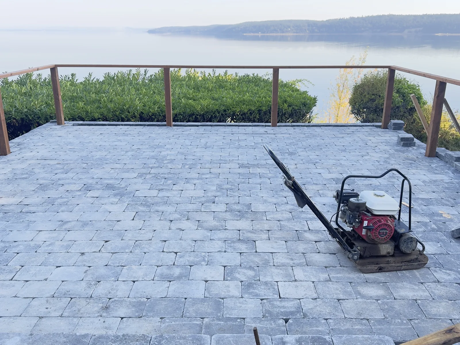 Paver patio with a water view and a plate compactor during installation