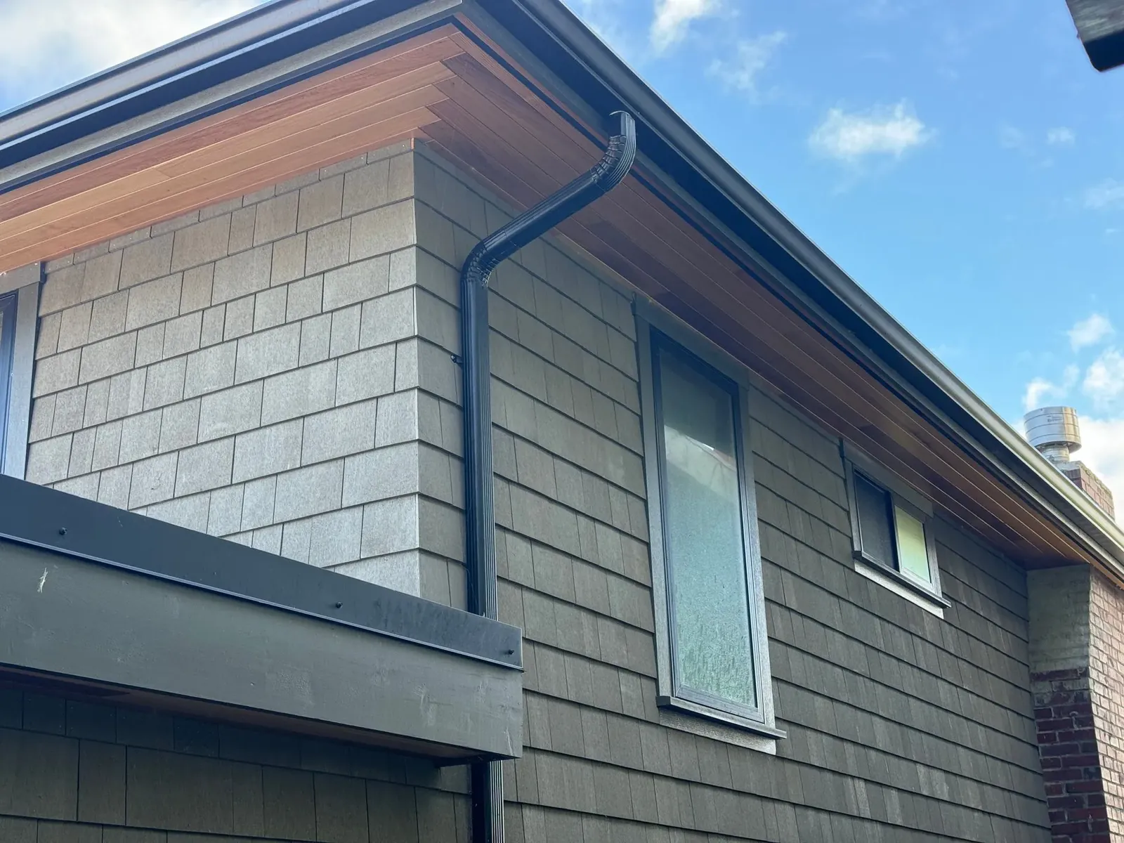 Shingle siding under a cedar soffit with a black gutter and downspout