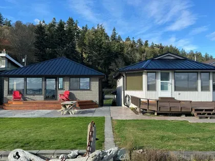 Two waterfront cottages with standing-seam metal roofs behind a lawn